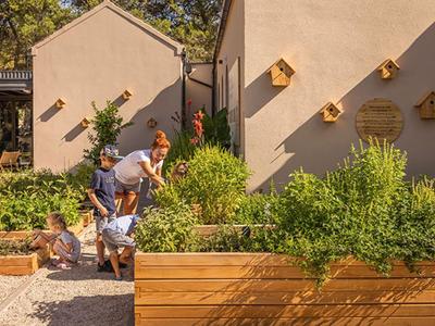 Famille avec enfants jouant à l'extérieur à côté d'un jardin avec des nichoirs sur un mur.