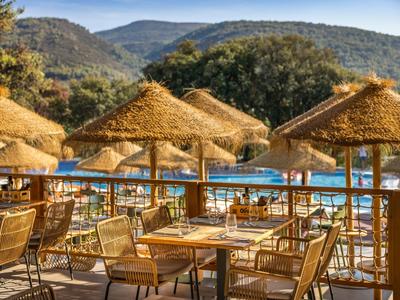 Sun terrace with thatched umbrellas and tables overlooking a pool area in the mountains.