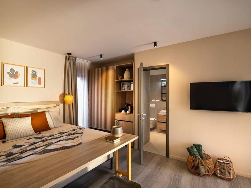 Modern hotel room with wooden furniture, bed, TV, and access to bathroom.