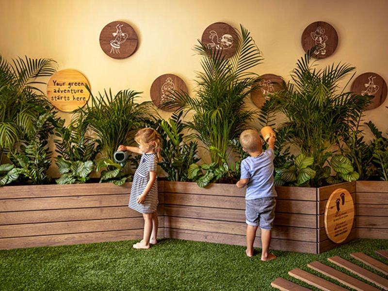 Two children in front of a cactus exhibit with plants and wooden containers in a garden.