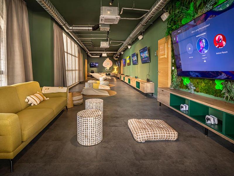 Modern lounge with sofas, TVs, and cozy atmosphere in green and yellow tones.