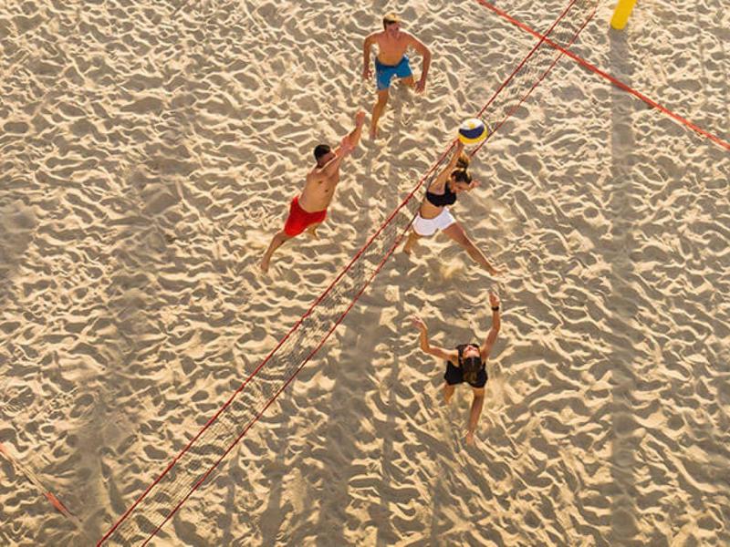 Group playing volleyball on sand with long shadows in sunlight.