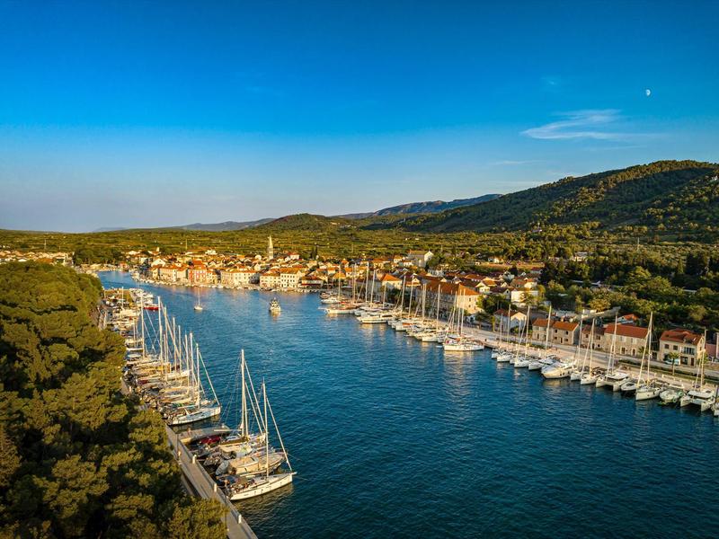 Harbor with sailboats along a river surrounded by hills and buildings under clear sky.
