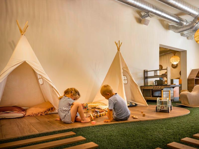 Children play in a cozy room with tipi tents on a green carpet.
