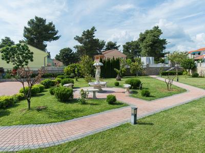 Jardin d'hôtel bien entretenu avec chemins, statue de buste et plantes vertes sous un ciel bleu.