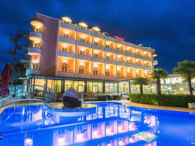 Hotel mit beleuchtetem Außenpool und Balkonen bei Nacht unter einem dunklen Himmel