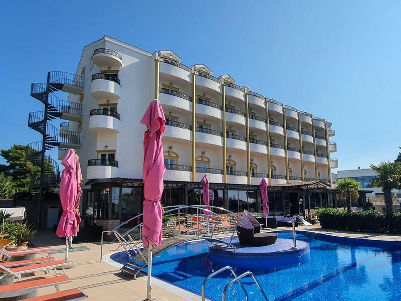 Moderner Hotelkomplex mit Pool, Liegestühlen und Sonnenschirmen an einem sonnigen Tag.