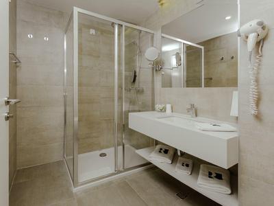 Modern hotel bathroom with glass shower, double sink, and wall-mounted hairdryer.