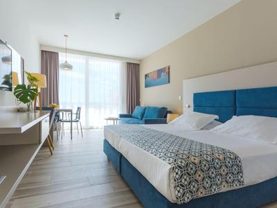 Modern hotel room with double bed, sofa, desk, and large window.