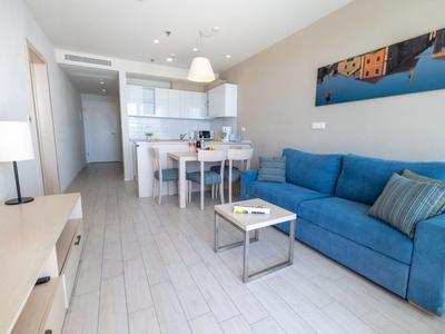 Modern living room with blue sofa, dining table, and open kitchen in bright apartment.