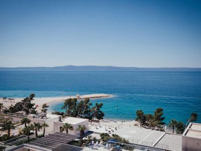 Blick auf einen Strand mit blauem Meer, Sand, Palmen und einem klaren Himmel.