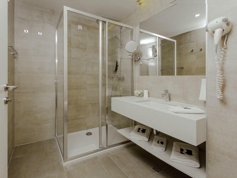 Modern hotel bathroom with glass shower, double sink, and wall-mounted hairdryer.