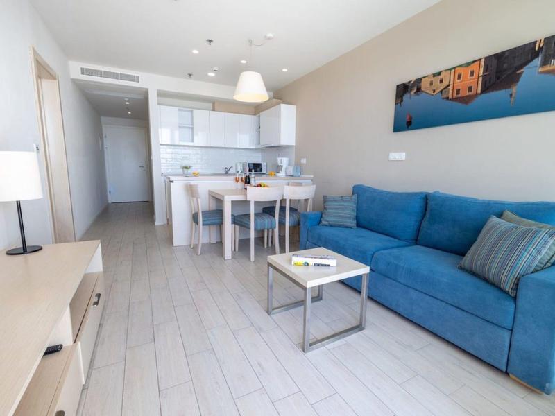 Modern living room with blue sofa, dining table, and open kitchen in bright apartment.