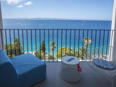 Balkon z niebieskimi fotelami, małym stolikiem i widokiem na morze przy czystym niebie.