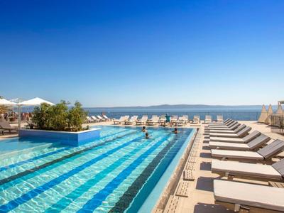 Piscine moderne avec chaises longues et vue sur la mer sous un ciel clair