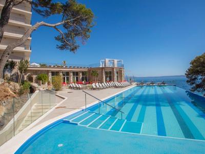 Hôtel moderne avec grande piscine extérieure et vue sur la mer sous un ciel bleu clair.