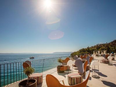 Terrasse ensoleillée avec des chaises modernes donnant sur la mer et une côte verdoyante.