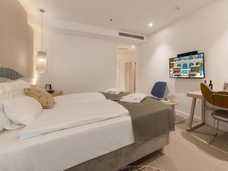 Nowoczesny pokój hotelowy z podwójnym łóżkiem, biurkiem, krzesłem i telewizorem na ścianie.