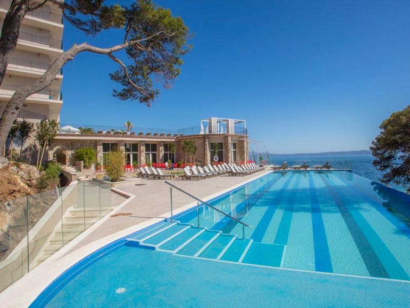 Basen typu infinity z widokiem na morze i leżakami w ośrodku hotelowym pod czystym niebem.