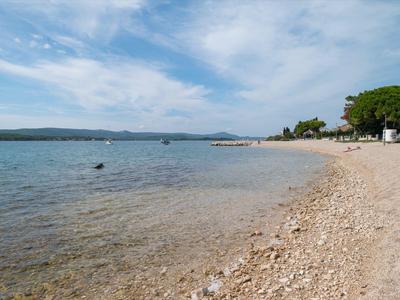 Spiaggia di ciottoli con acqua limpida e cielo nuvoloso in un paesaggio costiero tranquillo.