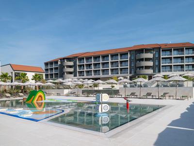 Moderní hotelový komplex s bazénem, slunečníky a čistou oblohou v pozadí