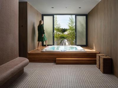 Moderní wellness místnost s dřevěným obložením, vířivkou na podiu a výhledem do zeleně.