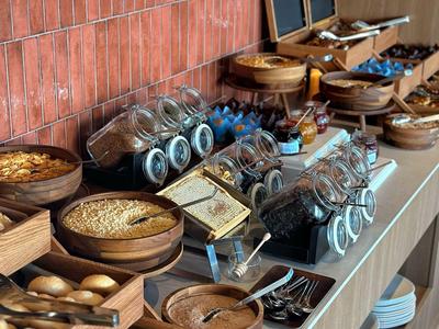 Bufet s různými snídaňovými možnostmi a sklenicemi před červenou cihlovou zdí.