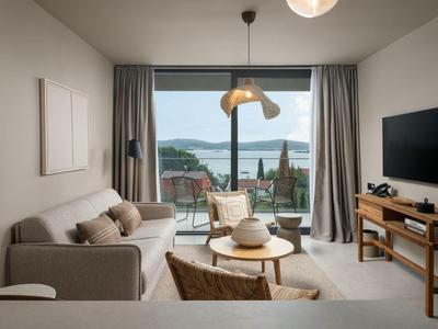 Sala de estar moderna con sofá y sillones, vista a la terraza y al mar a través de gran puerta corredera de vidrio.