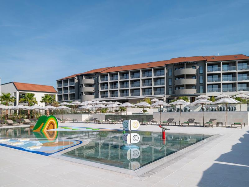 Moderní hotelový komplex s bazénem, slunečníky a čistou oblohou v pozadí