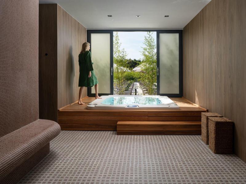 Moderní wellness místnost s dřevěným obložením, vířivkou na podiu a výhledem do zeleně.