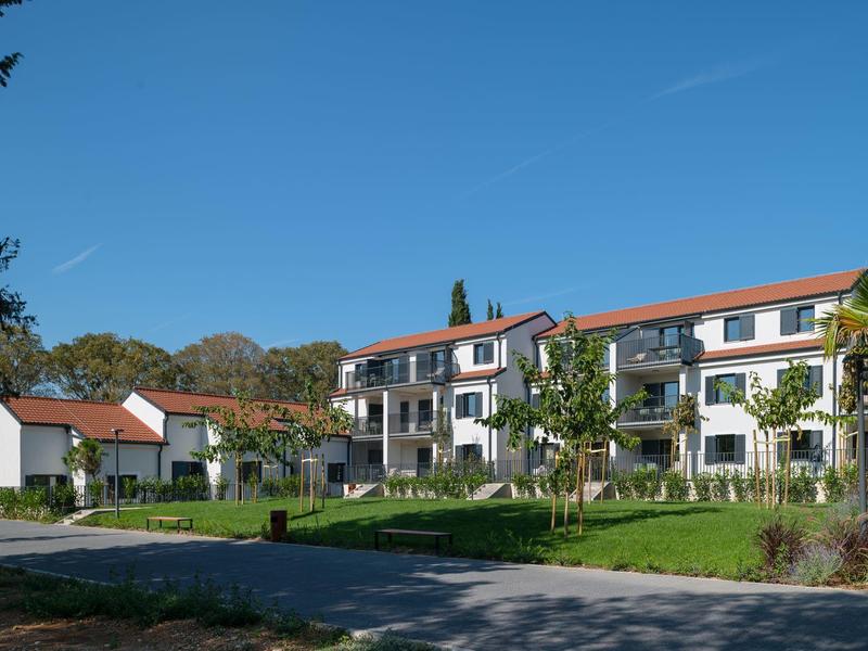 Moderní třípatrový hotelový komplex v zeleném prostředí s zahradou a posezením.