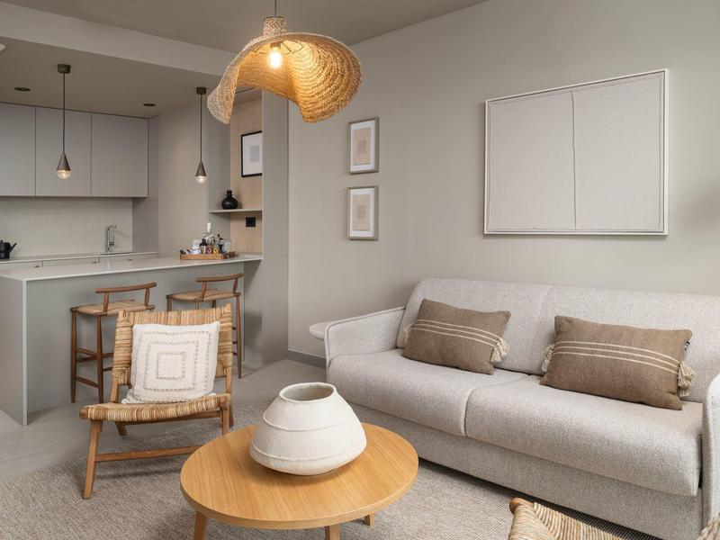 Moderní obývací pokoj s pohovkou, křeslem, kulatými stolky a otevřenou kuchyní v pozadí.