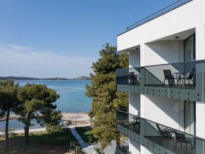 Balconi di un hotel bianco con vista sul mare e alberi sullo sfondo.