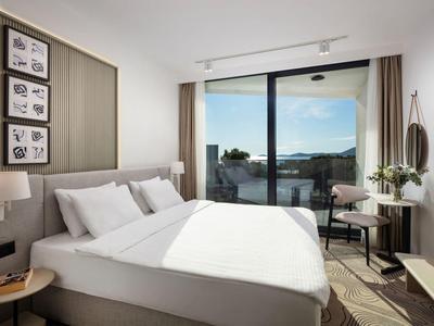 Nowoczesny pokój hotelowy z dużym łóżkiem, balkonem i widokiem na morze przy czystym niebie.