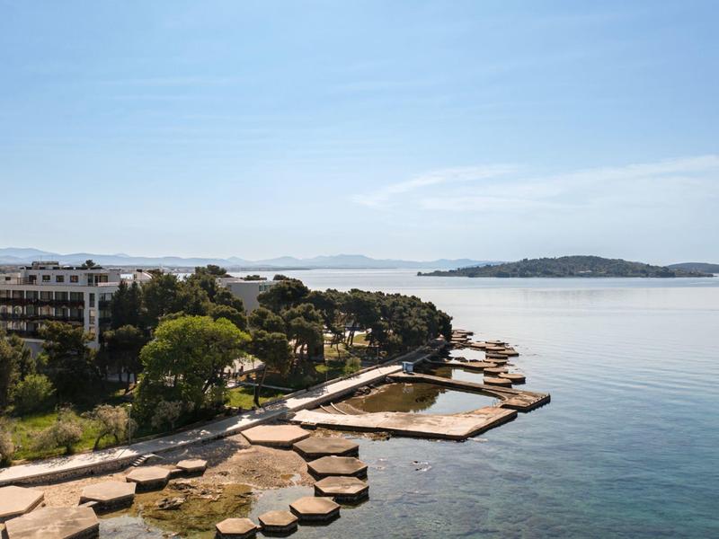 Linia brzegowa z kamieniami, zielonymi drzewami i budynkiem nad morzem pod czystym niebem