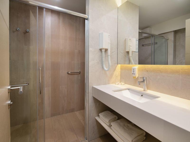 Salle de bain moderne avec douche en verre, grand lavabo et serviettes en dessous.