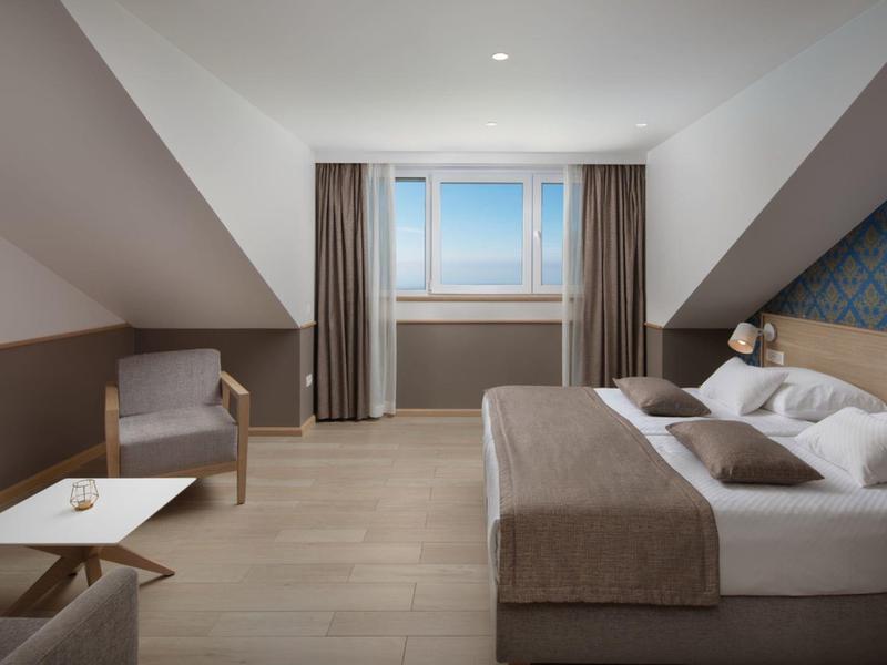 Chambre d'hôtel moderne avec lit double, fauteuil, fenêtre et décoration simple.