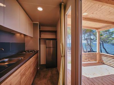 Modern kitchen area with wooden elements and access to a covered terrace overlooking the sea.