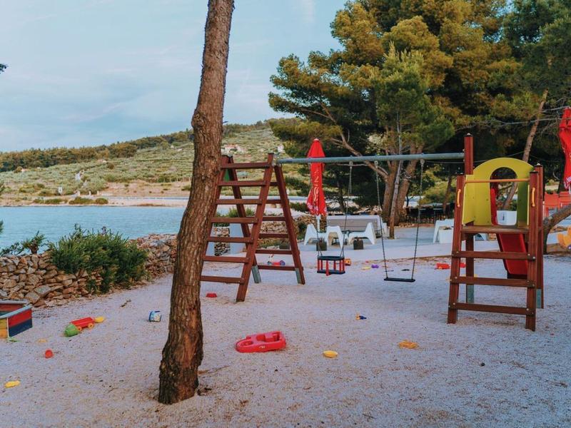 Children's playground with swings and slide on a beach with trees in the background.