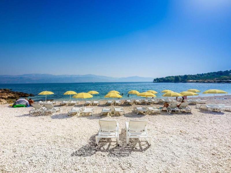 Beach with yellow umbrellas and white sun loungers by clear sea and blue sky.