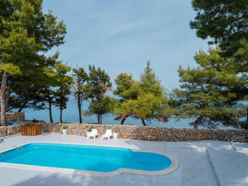 A blue pool with white lounge chairs, surrounded by pine trees and sea view.