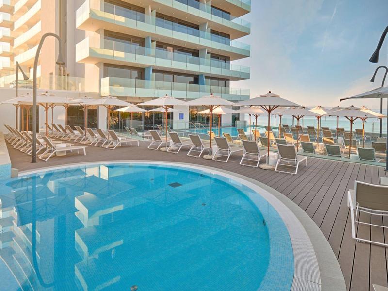 Nowoczesny basen na zewnątrz z leżakami i parasolami obok budynku hotelu