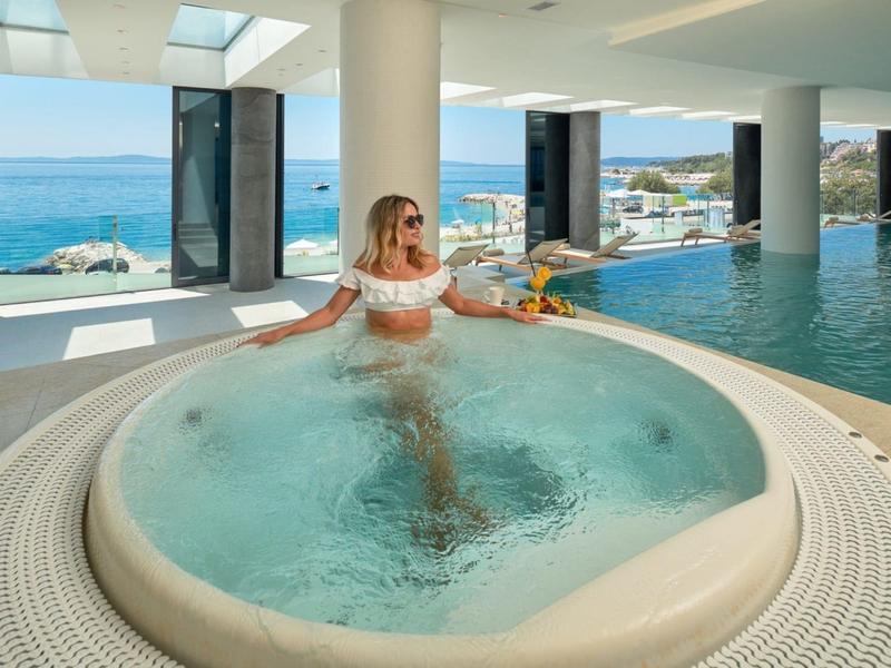 Kobieta relaksująca się w jacuzzi z widokiem na morze i kryty basen.