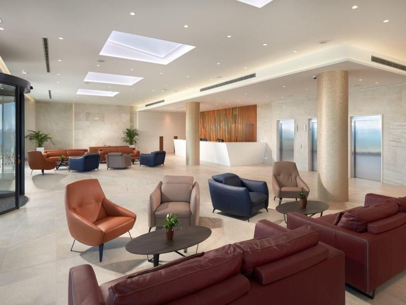 Nowoczesna przestrzeń lounge w hotelu z wygodnymi fotelami i sofami w ciepłych tonach, jasnym oświetleniem i otwartym układem.