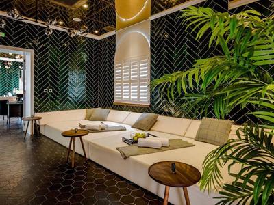 Nowoczesna przestrzeń wypoczynkowa z sofą, zielonymi płytkami i dużymi roślinami w hotelu.