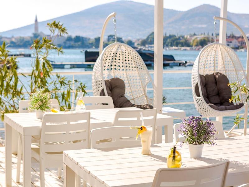 Przytulny taras z białymi meblami i wiszącymi fotelami z widokiem na morze i góry.