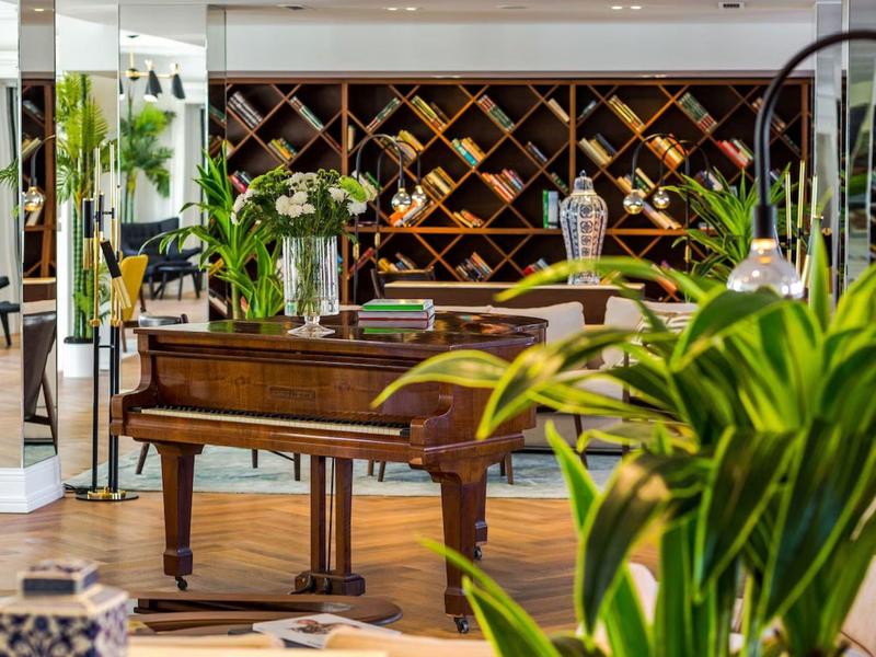 Elegancki obszar fortepianu z drewnianą półką na wino i zielonymi roślinami w nowoczesnym wnętrzu hotelu.