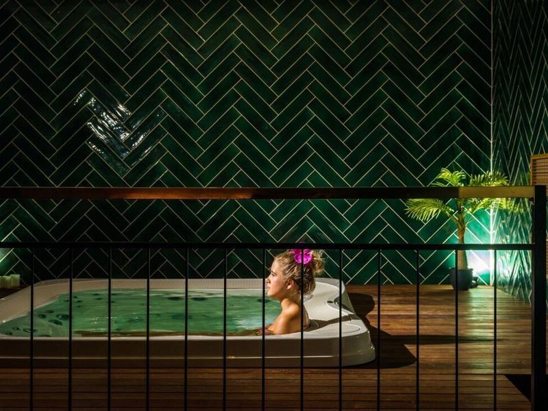 Kobieta relaksuje się w oświetlonym jacuzzi w nowoczesnym pomieszczeniu z zielonym tłem.