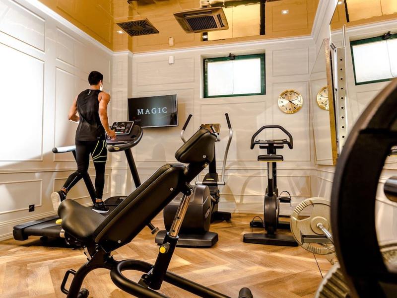 Nowoczesna siłownia z jasnymi ścianami, kilkoma maszynami do ćwiczeń i osobą na bieżni.