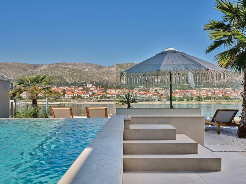 Nowoczesny basen z leżakami i parasolem z widokiem na miasto i góry.